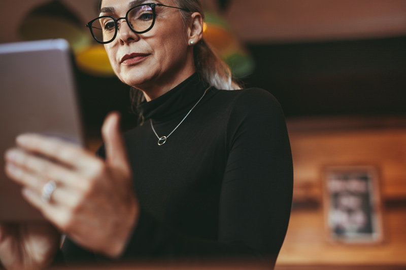 A senior businesswoman with glasses reading an article on her iPad.