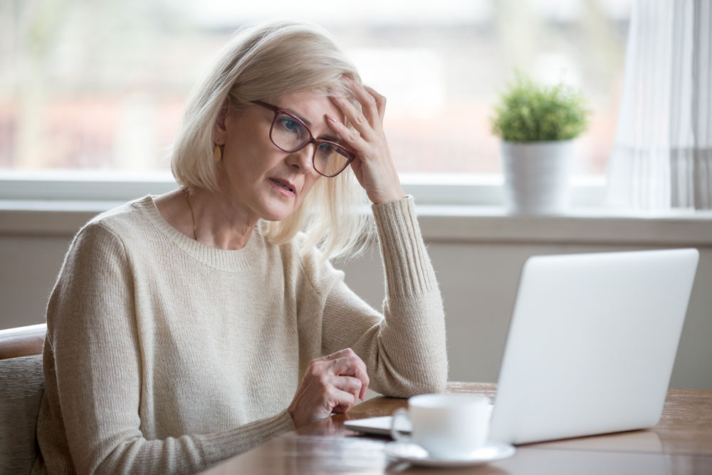 A senior woman with glasses, looking curious as she looks at her laptop.