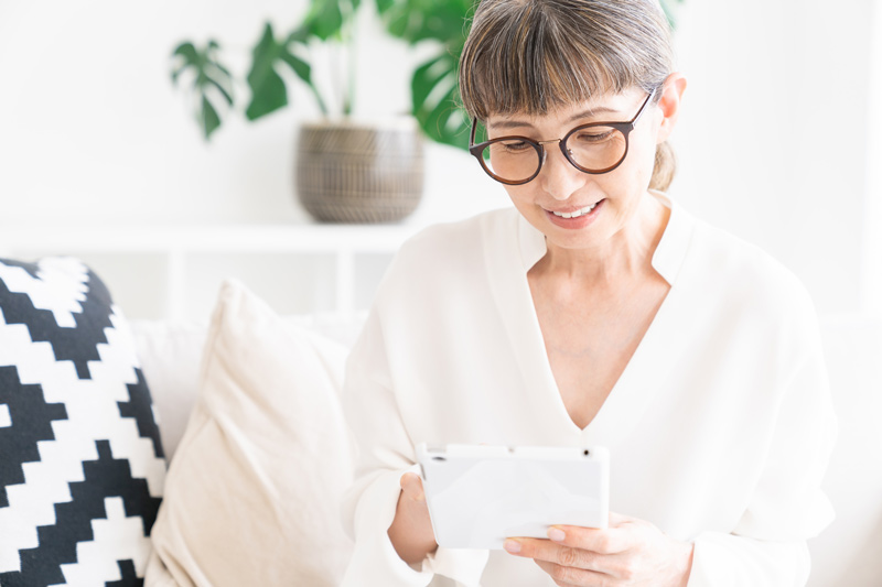 A senior Asian woman, wearing glasses, looks at her phone.