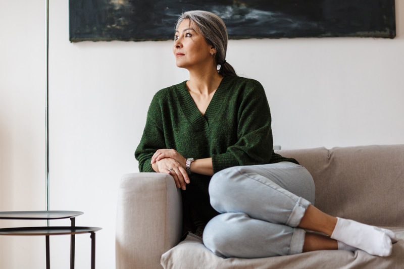 A senior woman sitting on a sofa, looking out the window and wondering if the early stages of cataracts can be reversed.