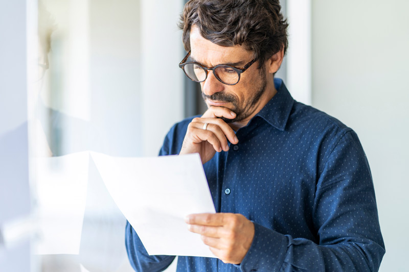 A senior man with glasses, carefully examining paperwork.